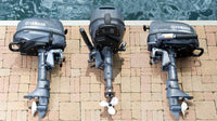 Drie Yamaha buitenboordmotoren naast elkaar opgesteld aan de waterkant, met zichtbaar compact ontwerp en helmstokbediening, geschikt voor rubberboten en kleine boten.
